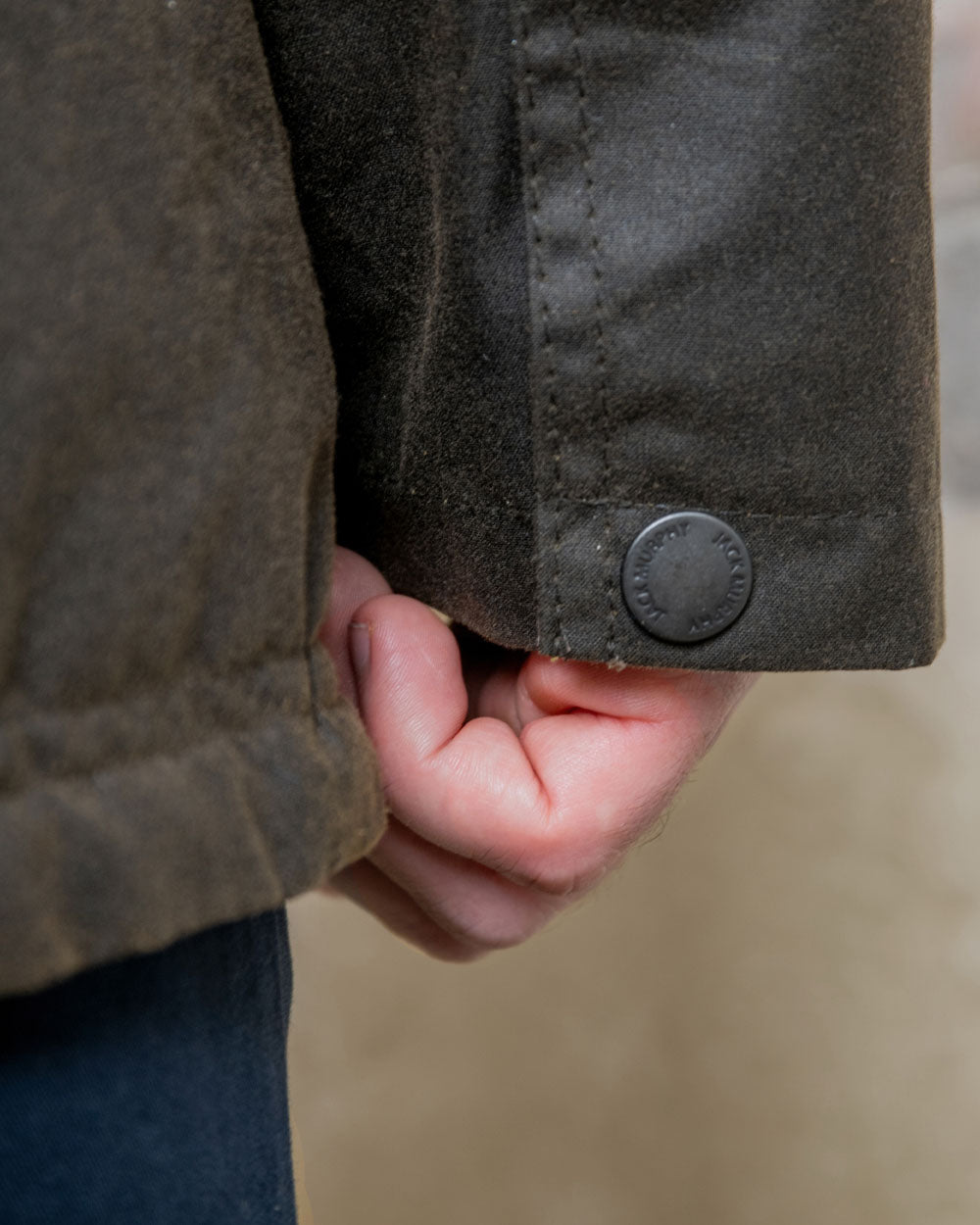 Olive coloured Jack Murphy Archie Wax Jacket Sleeve Button closeup on blurry background 