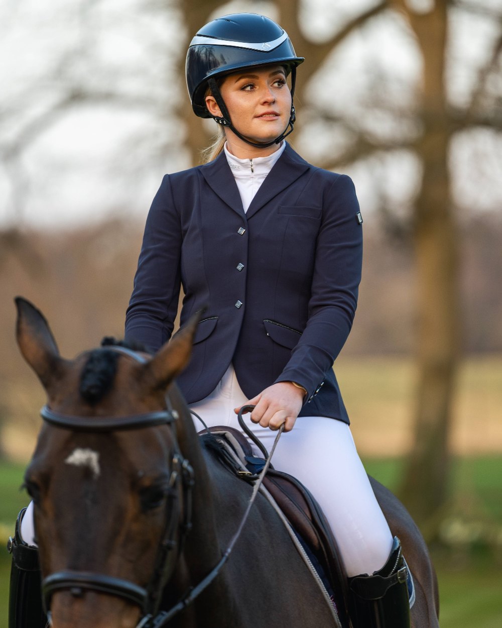 Navy coloured LeMieux Dynamique Show Jacket with horse in background 
