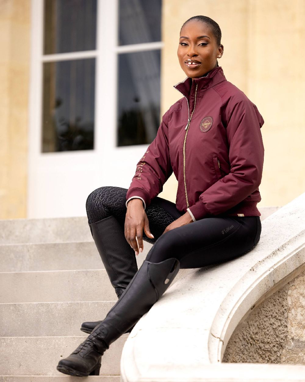 Burgundy coloured LeMieux Elite Crew Jacket with building in background 