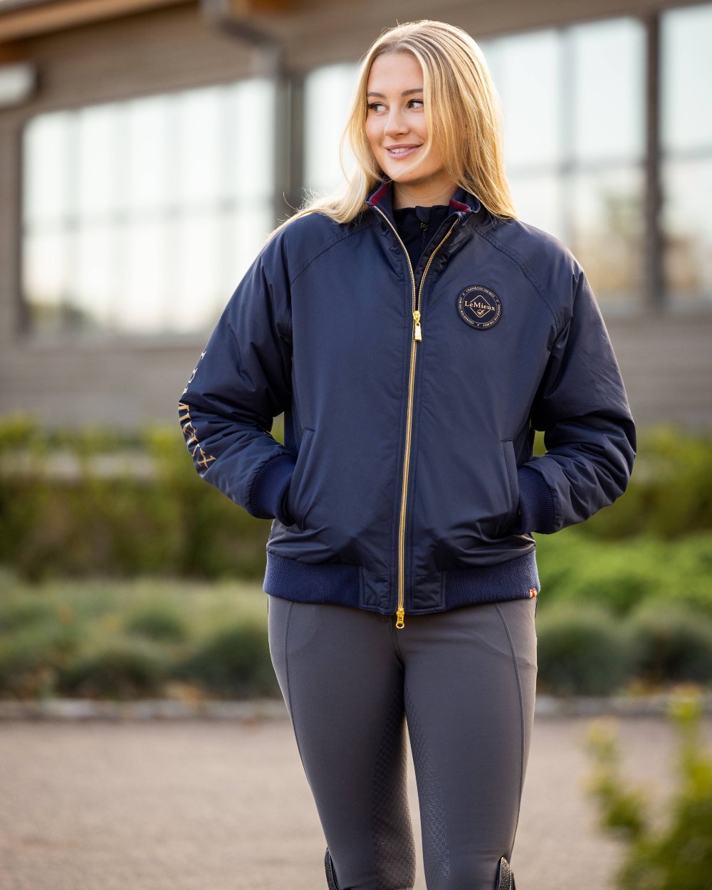 Navy coloured LeMieux Elite Crew Jacket on blurry building background 