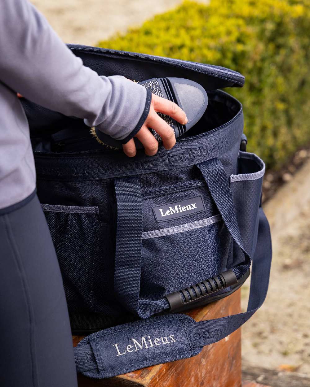 Navy coloured LeMieux Grooming Bag with hedge in background 