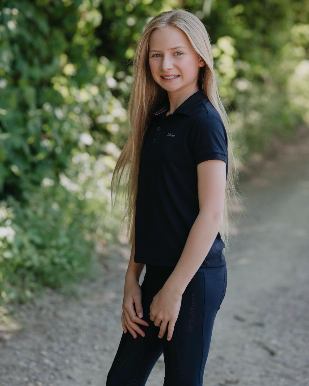 Navy coloured LeMieux Junior Pro Polo Shirts on green background 