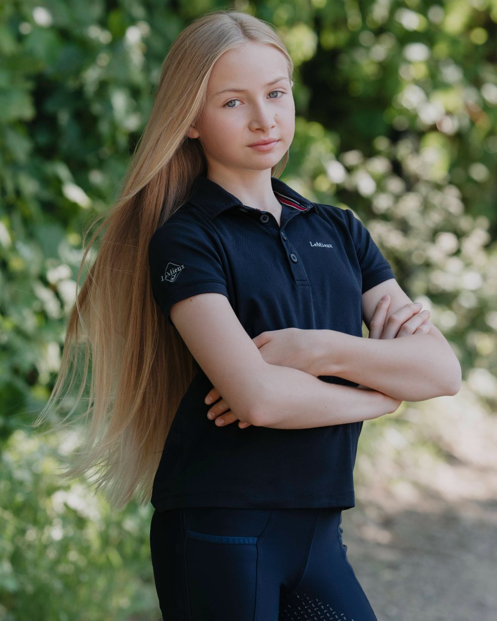 Navy coloured LeMieux Junior Pro Polo Shirts on green background 