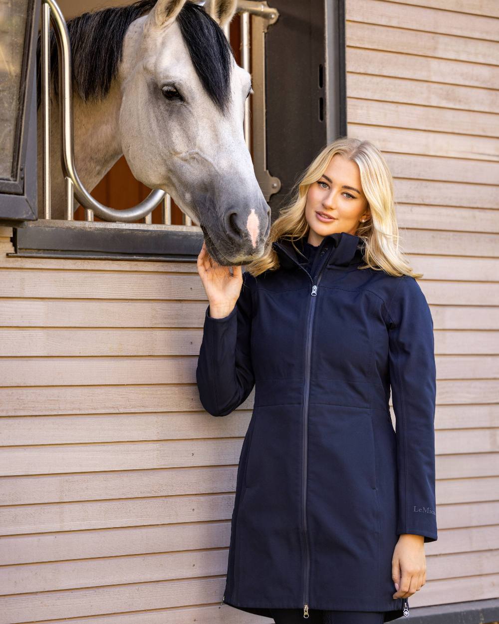 Navy coloured LeMieux Maisie Lightweight Riding Jacket with horse in background 