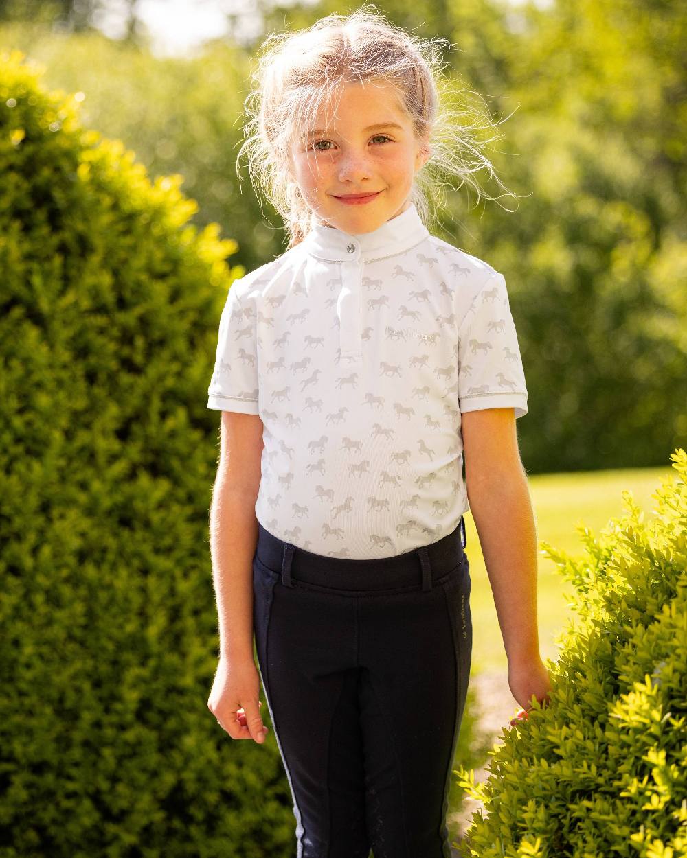 White coloured LeMieux Mini Bella Show Shirt with green bush in background 