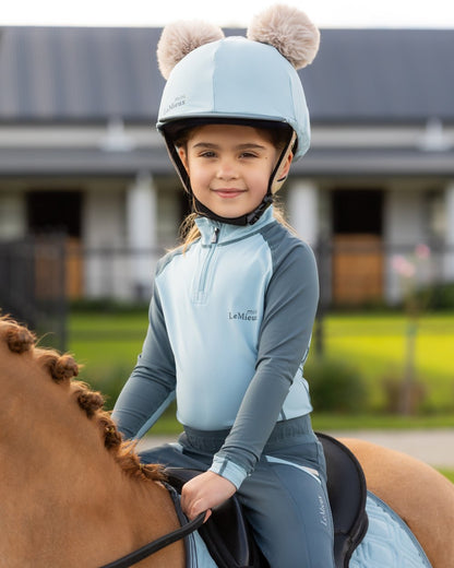 Glacier Coloured LeMieux Mini Double Pom Hat Silk On A Outer Yard Background 