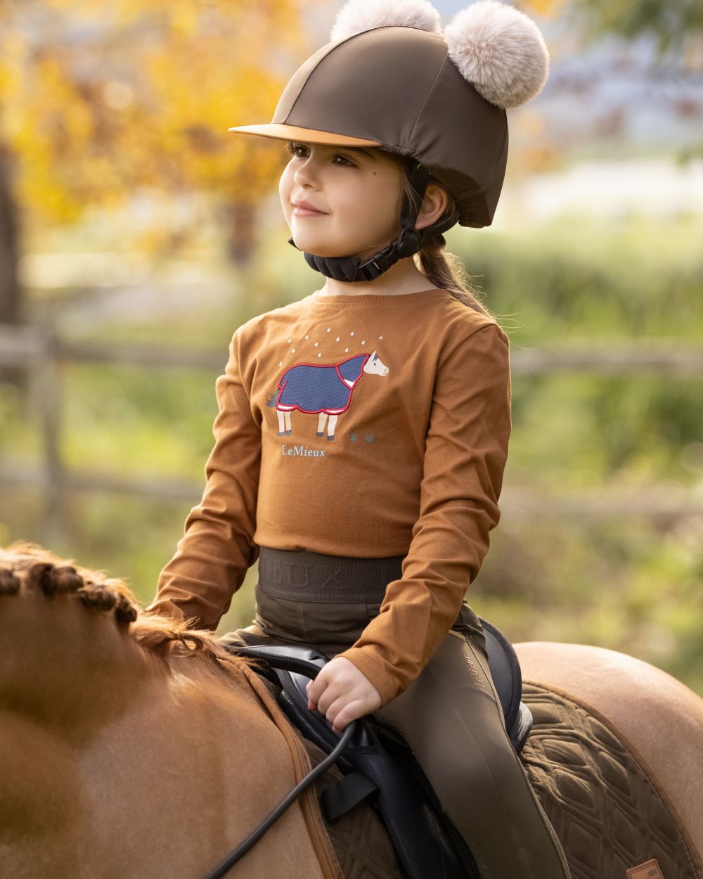 Ginger Coloured LeMieux Mini Jessie Long Sleeve Top On A Outer Yard Background 