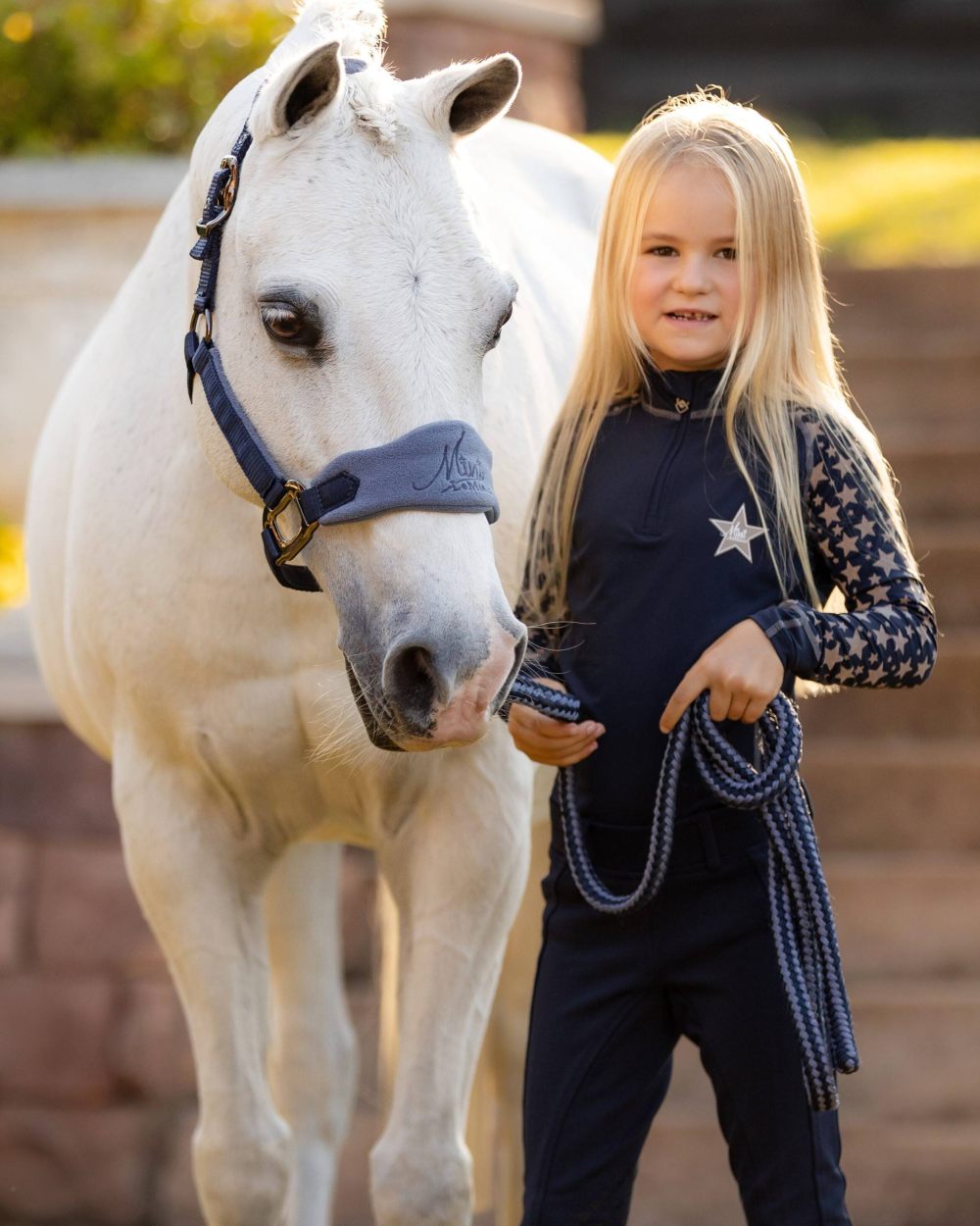 Indigo coloured LeMieux Mini Reflective Print Base Layer with horse in background 