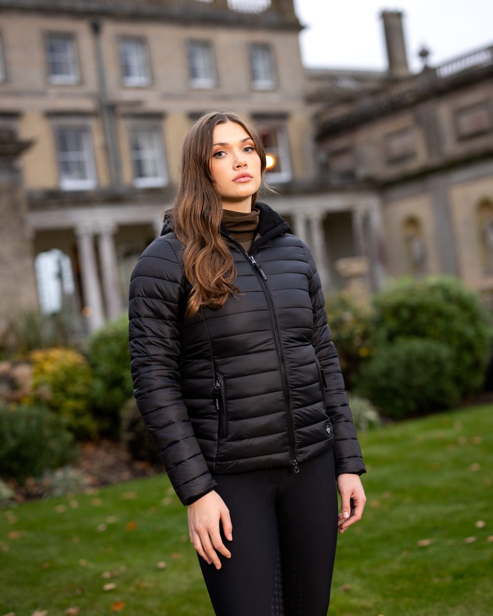 Black Coloured LeMieux Tilly Hooded Puffer Jacket On A Outer Yard Background 