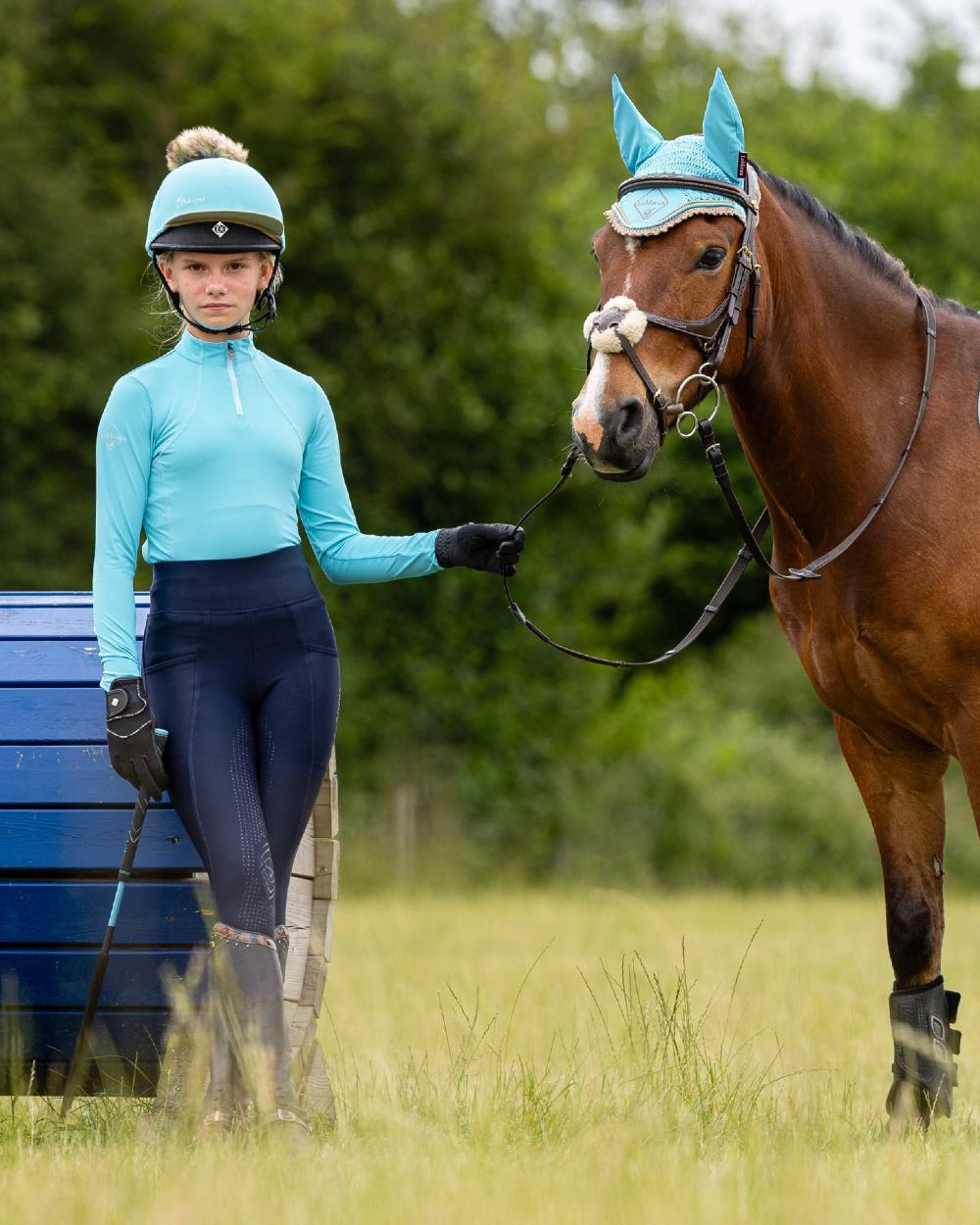 Azure coloured LeMieux Young Rider Base Layer with trees in background 