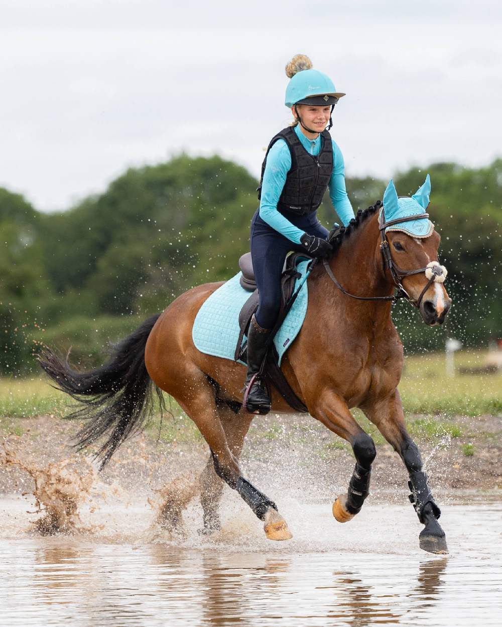 Azure coloured LeMieux Young Rider Base Layer with water in background 