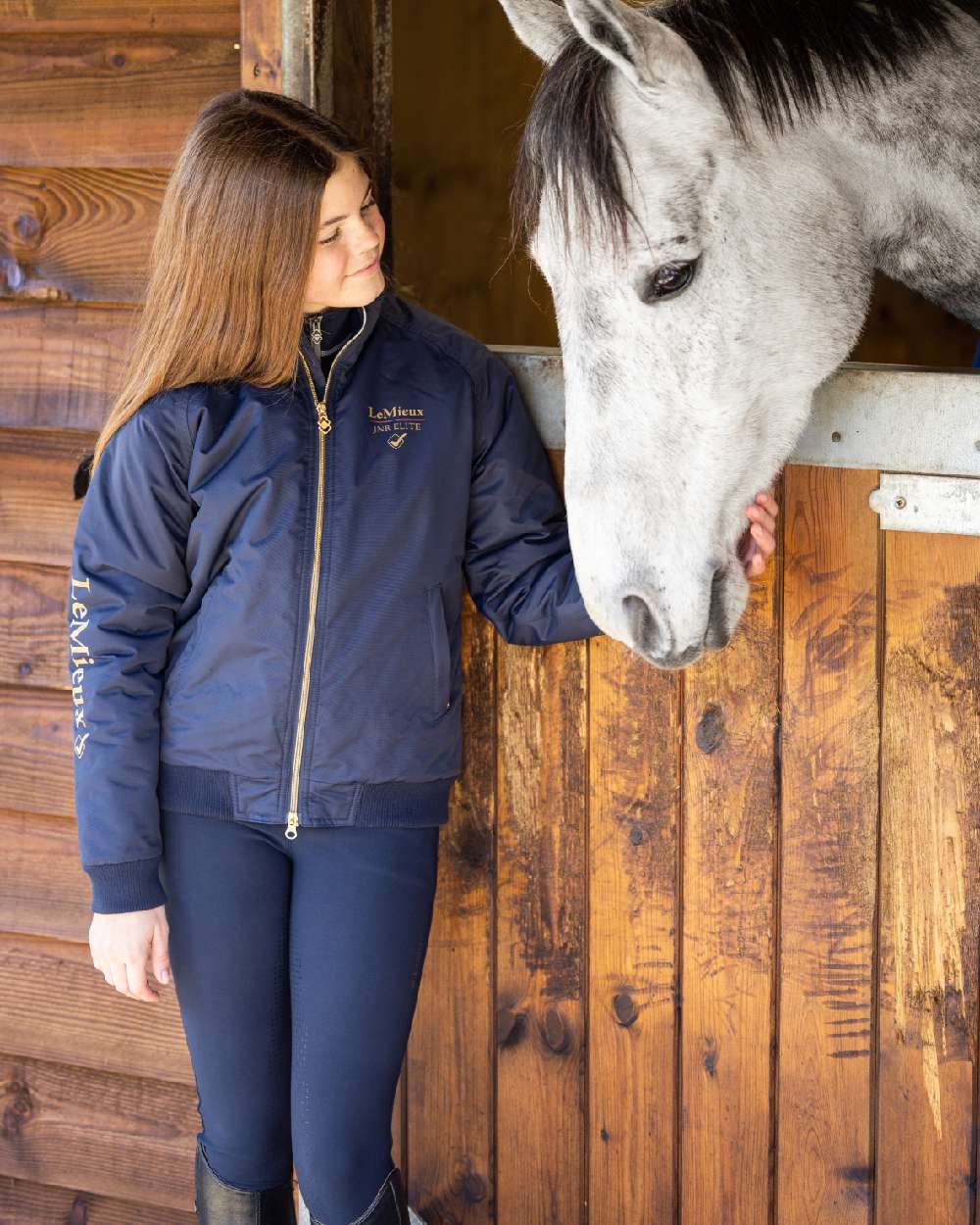 Navy coloured LeMieux Young Rider Elite Team Jacket with horse in background 