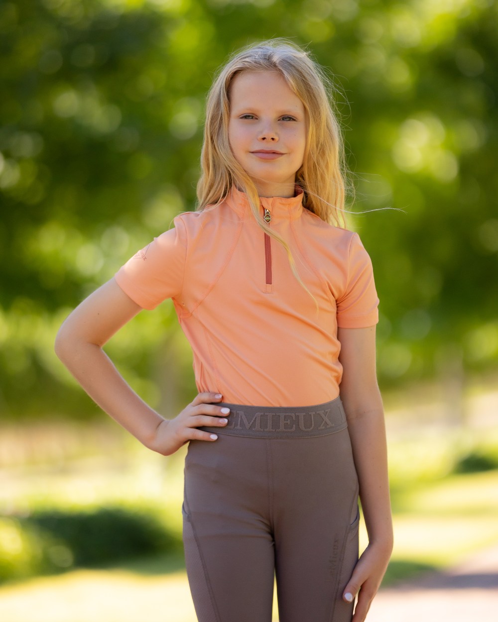 Sherbet coloured LeMieux Young Rider Short Sleeve Base Layer with leaves in background 