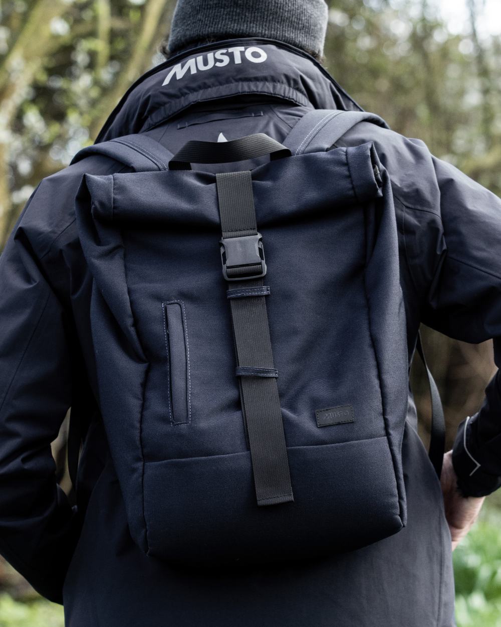 Navy Coloured Musto Canvas Roll Top Bag On A Coastal Background