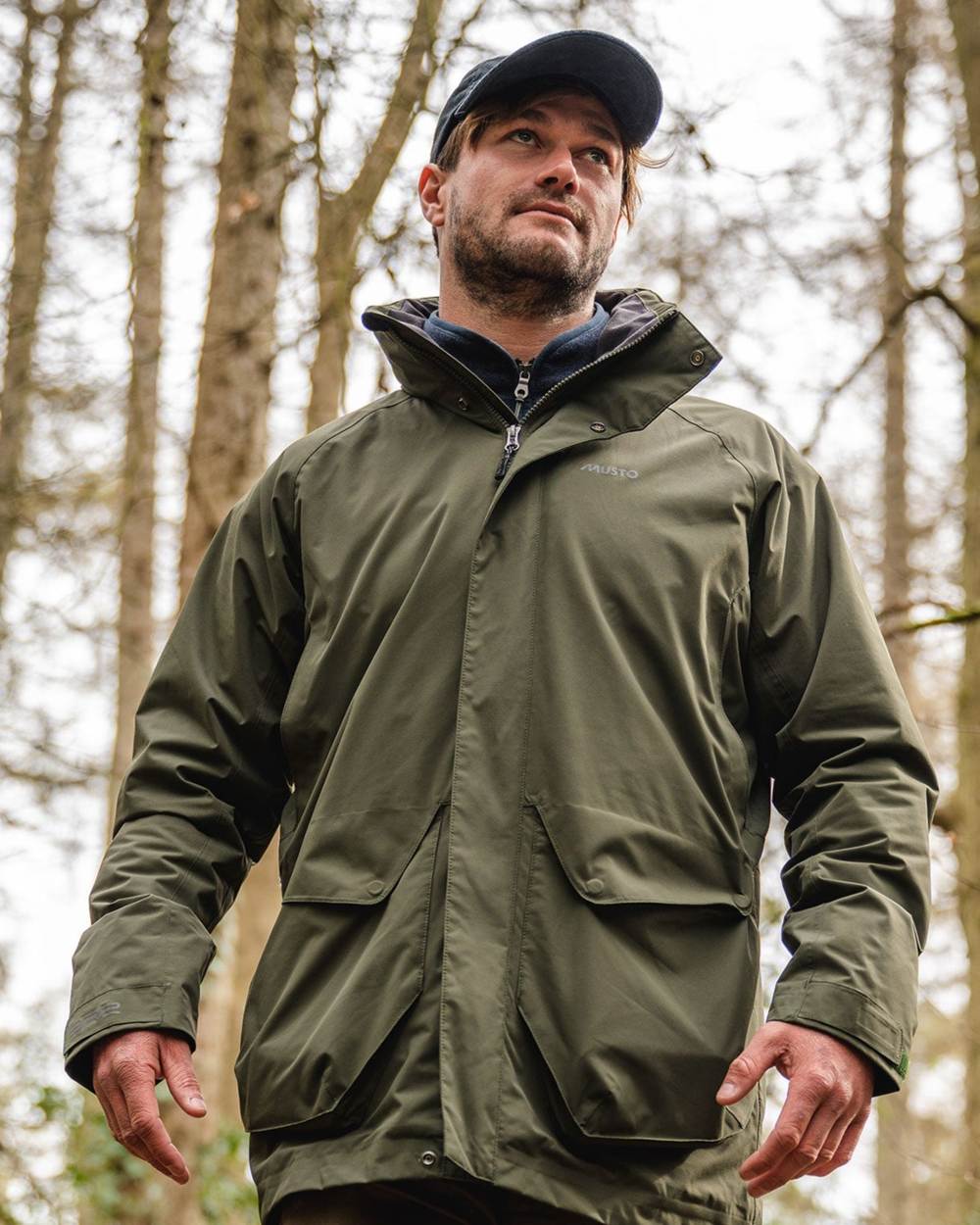 Deep Green coloured Musto Fenland Jacket 2.0 on forest background 