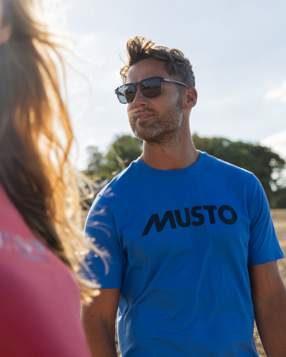 Nebulas Blue Coloured Musto Logo Cotton Tee on Beach Background
