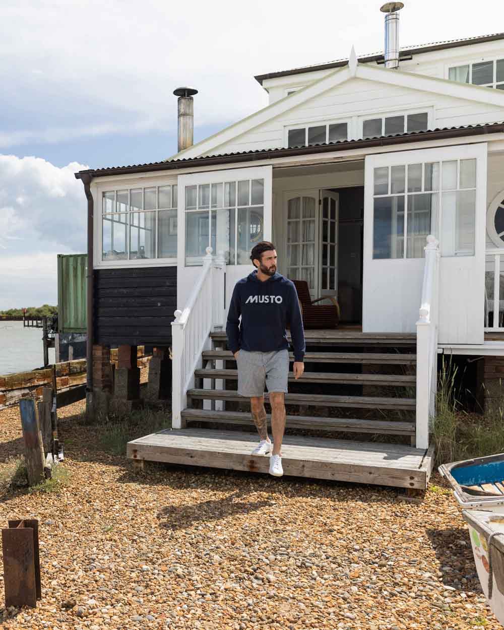 Navy coloured Musto Mens Logo Hoodie on Lake Cabin background 