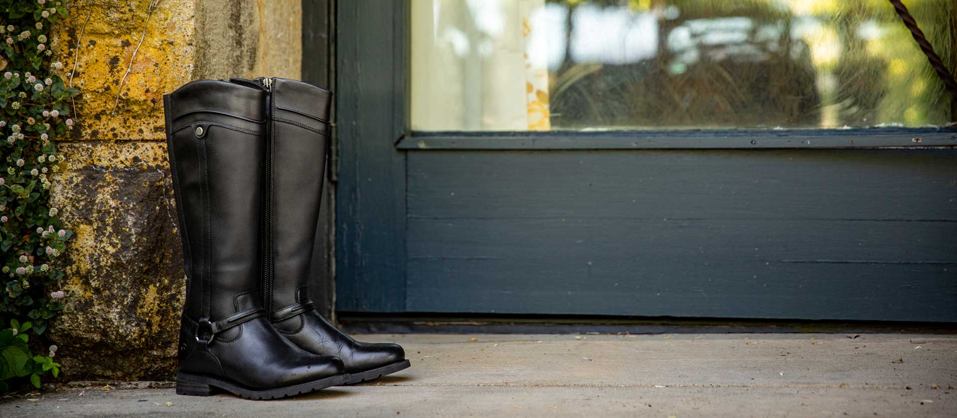 Black wellies sitting on the ground next to a stone wall and a green door