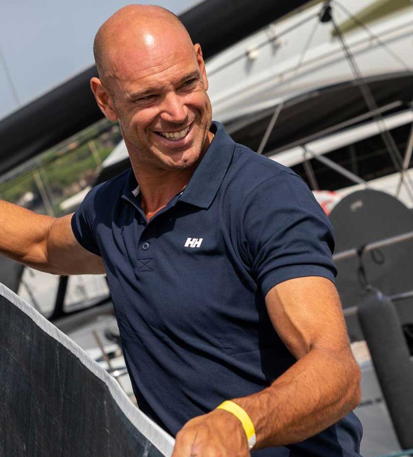 Man wearing Navy Blue polo shirt with boat in background.