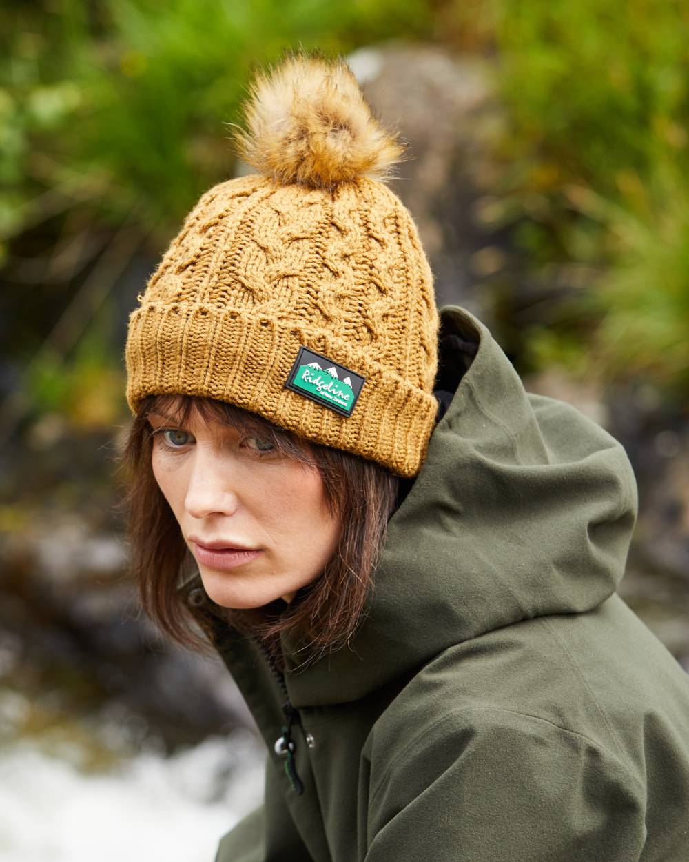 Ochre Coloured Ridgeline Nordic Fleck Bobble Hat On A Forest Background 