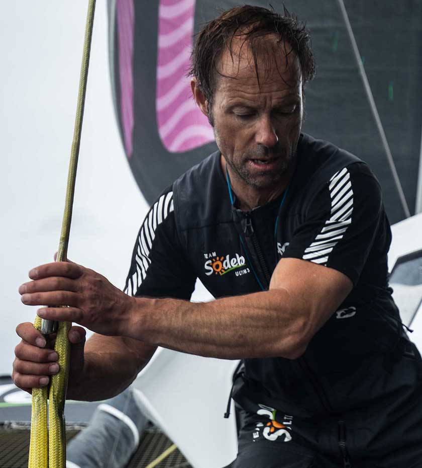 Sailing Baselayers | Yacht crew member wears black Helly hansen Base layer T-shirt top with sails and ropes in the background.