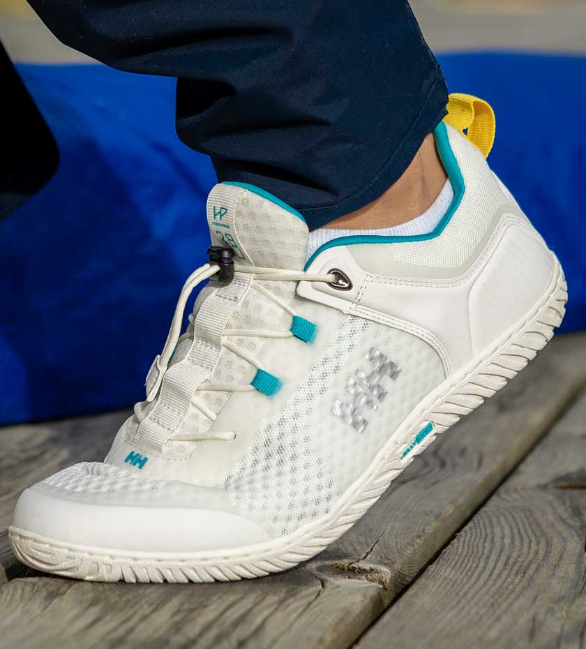 All White Sailing Trainer with laces and blue trim on a wooden boat deck.