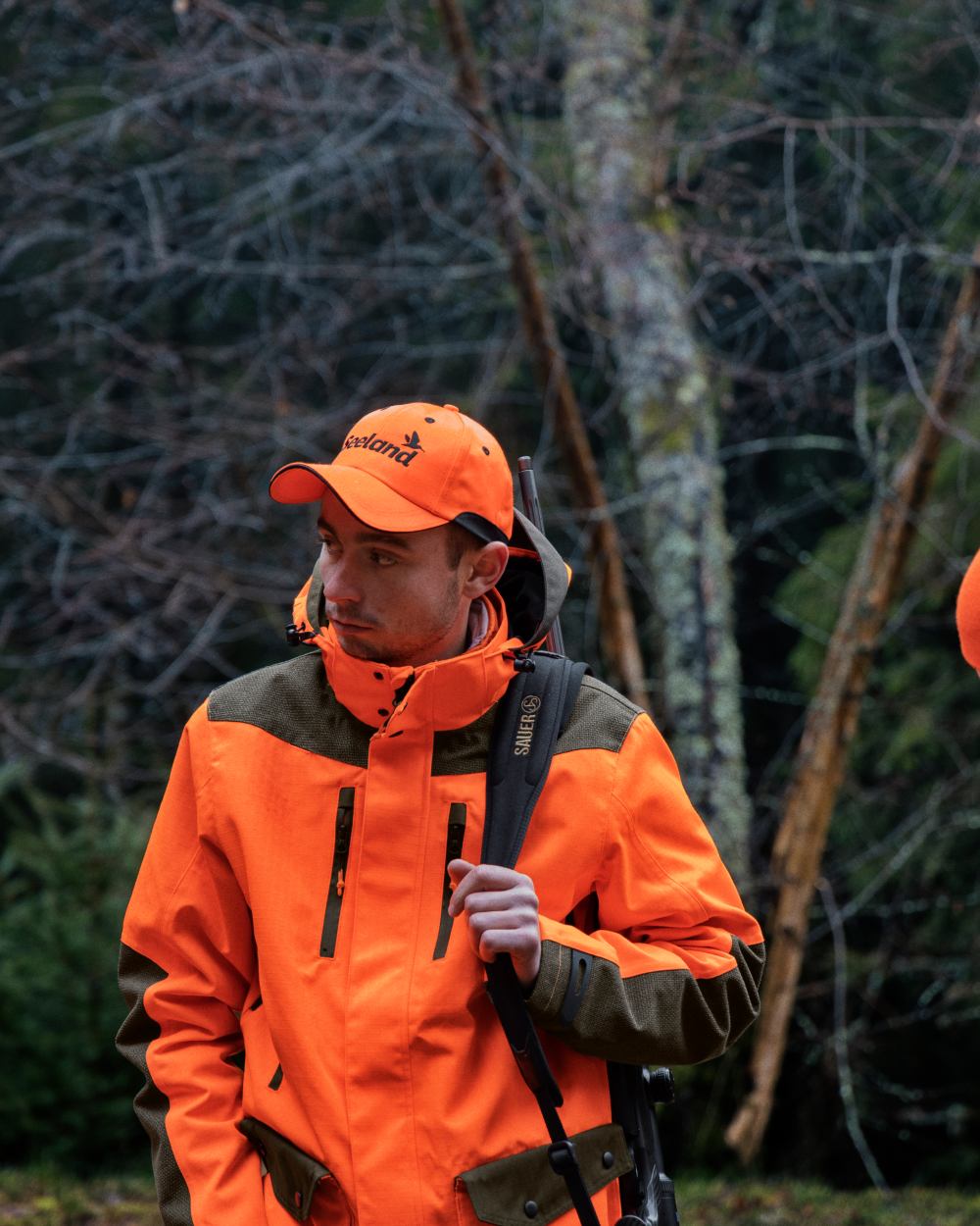 Pine Green/Hi-Vis Orange Coloured Seeland Venture Rover Jacket On A Forest Background