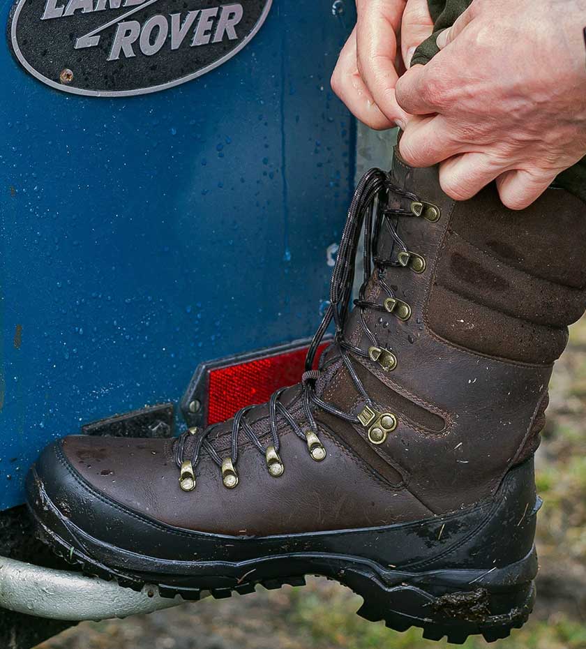 Shooting and Hunting Boots and Wellingtons. Brown leather lace up boots beside a blue land Rover.