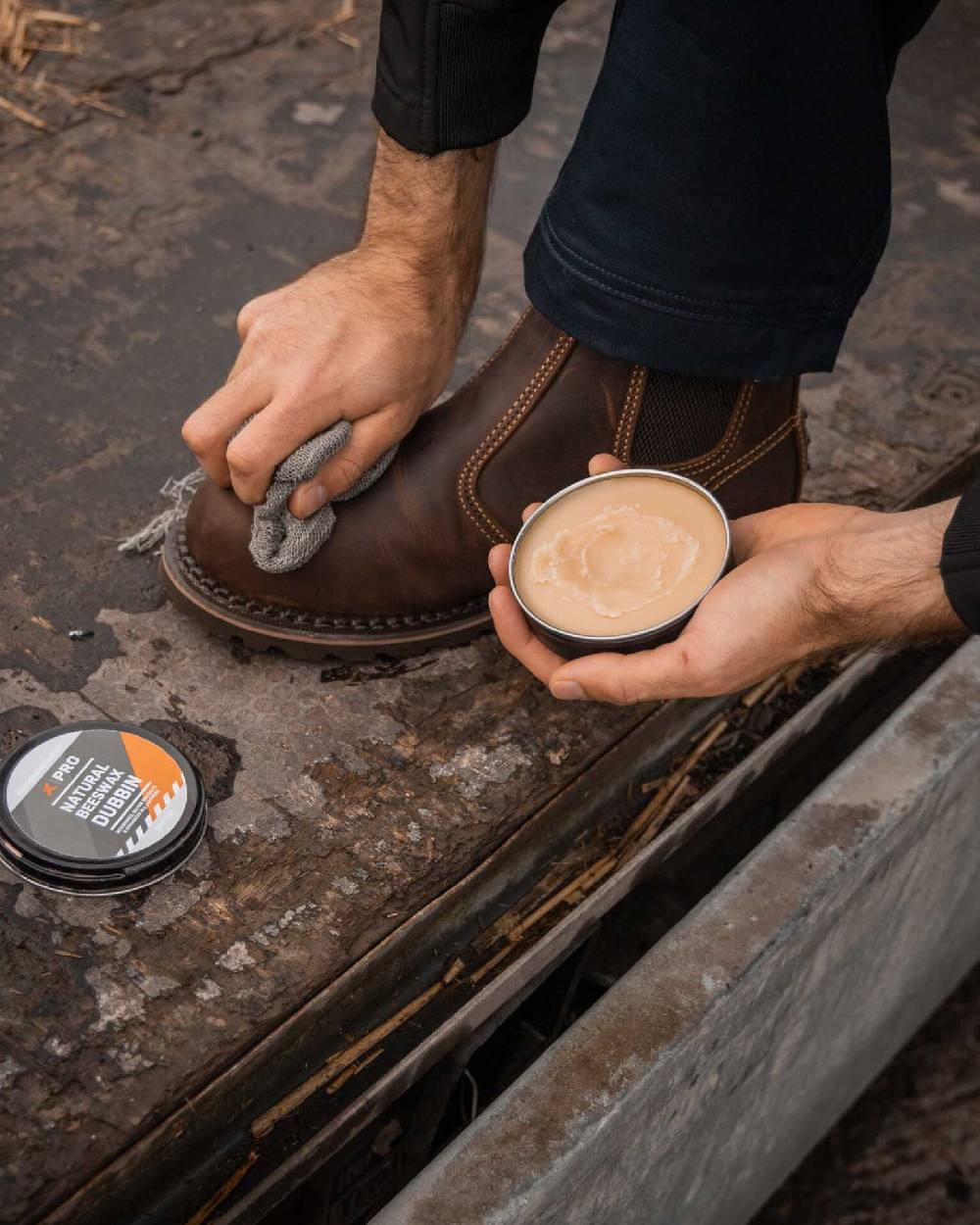 Person applying Xpert Pro Wax beeswax boot dubbin to brown leather work boots outdoors